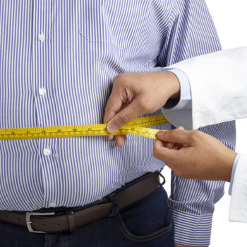 A doctor measures an overweight man's waist using a tape measure.