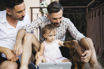 Couple with daughter and dog on balcony using digital tablet