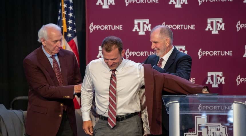 Texas A&M Interim Director of Athletics R.C. Slocum (left) and President Michael K. Young gift a maroon jacket to incoming Director of Athletics Ross Bjork.