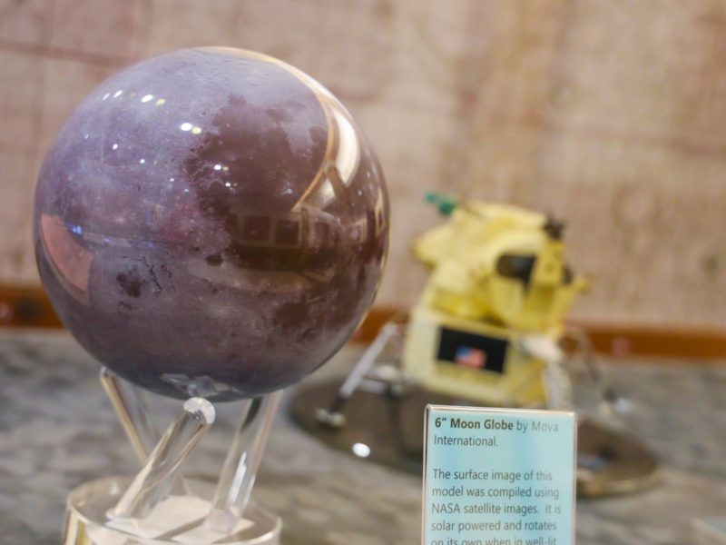 A small model of the moon and a miniature model of a lunar module sit next to each other in a display case.