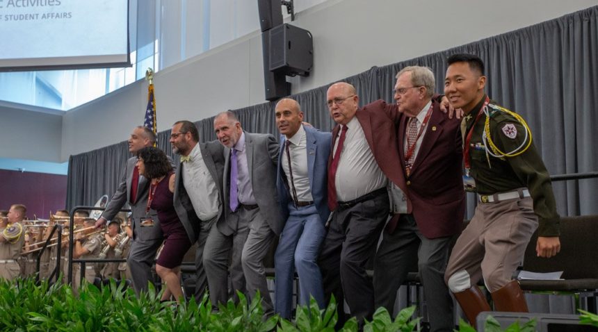 University officials and donors link arms on a stage during a ceremony for the Music Activities Center