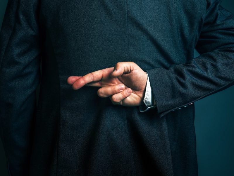 Lying and cheating businessman holding fingers crossed behind his back