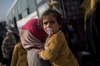 A young girl is carried by her mother as they board a bus after fleeing conflict in Iraq