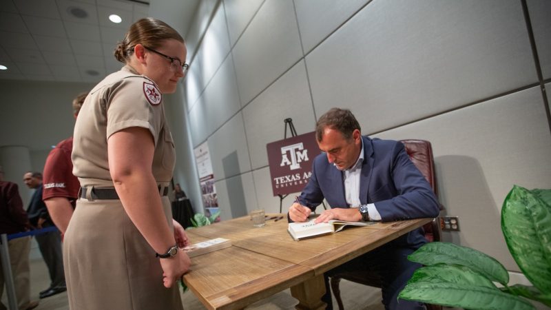 Author Alex Kershaw sits at a table as he signs a student's book