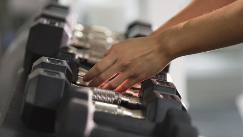 Hands of woman reaching for dumbbells