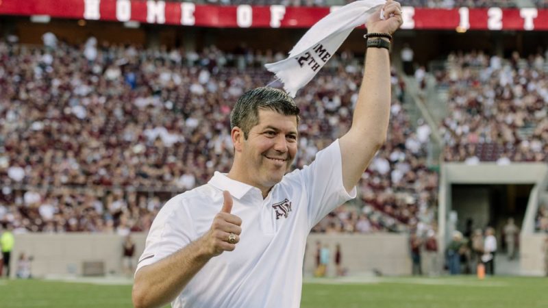 a photo of Fernando Palomo at Kyle Field wearing an Aggie shirt, carrying a 12th man towel, and giving the Gig Em thumbs up