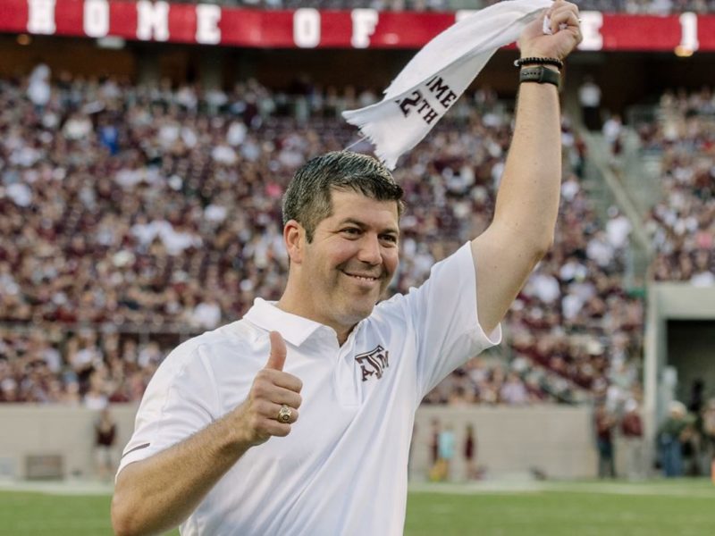 a photo of Fernando Palomo at Kyle Field wearing an Aggie shirt, carrying a 12th man towel, and giving the Gig Em thumbs up