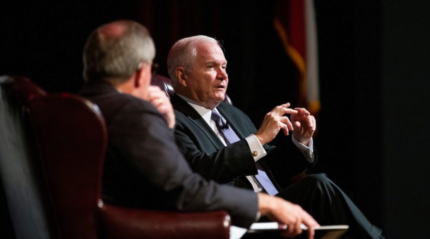 Former Texas A&M president Robert Gates talks on a stage while seated next to Bush School dean Mark Welsh