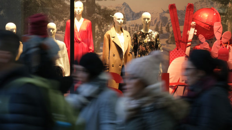 People walk past mannequins in a clothing retailer display window