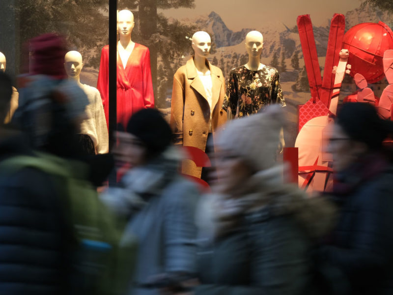 People walk past mannequins in a clothing retailer display window
