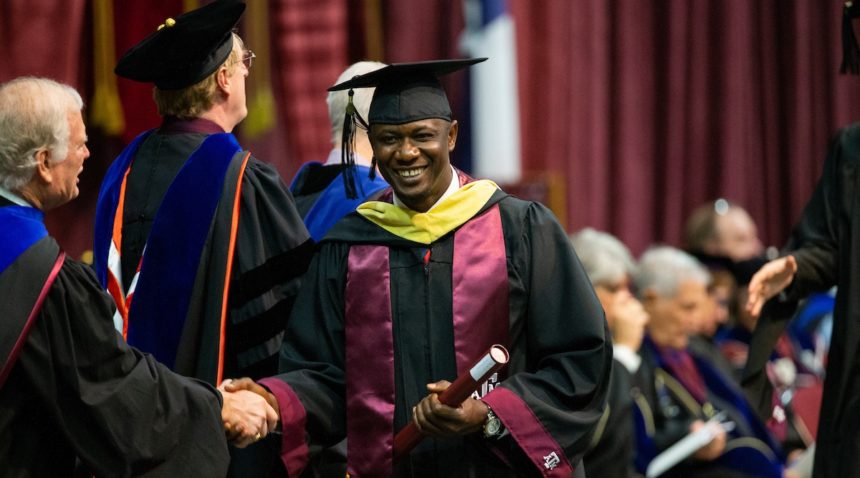 a student holding a diploma shakes hands with faculty as he crosses the stage