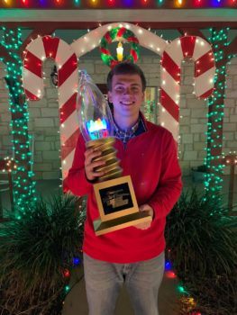 Student standing with trophy in front of christmas lights on a home