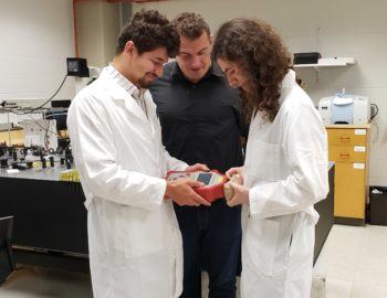Mark Krimmer, an undergraduate student (left), Dmitry Kurouski (center) and Charles Farber, a graduate student (right) demonstrate how to scan grain for nutrient content with a handheld Raman spectrometer. 