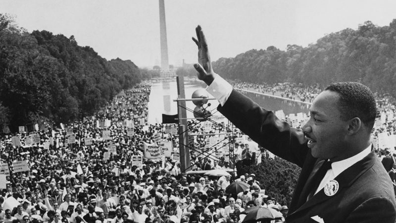 A black and white photo of Dr. King waving to the crowd at the March On Washington