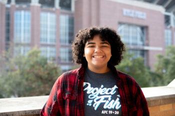a student smiles in front of kyle field in the background