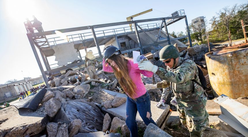 girl wearing pink shirt and hard hat walking over rubble with man in army fatiues