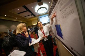 a student points at a poster of her research while a woman looks on