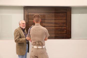 mikeual perritt standing in front of his wood sculpture with a cadet in uniform