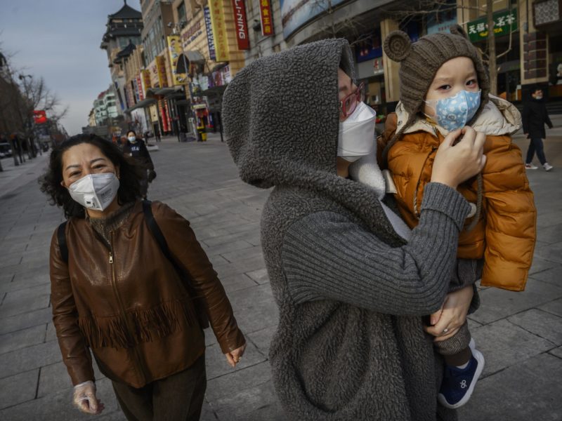 a chinese woman and her child wear protective masks in a nearly empty commercial street in beijing