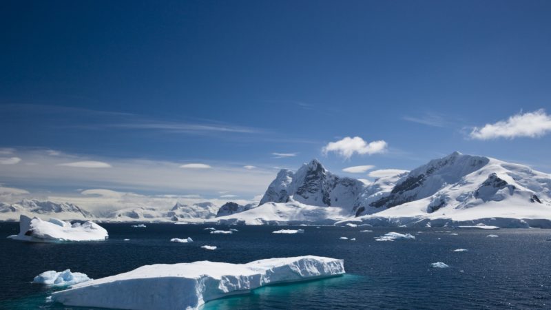 An iceberg floating on the water in antarctica, with snowy mountains in the background