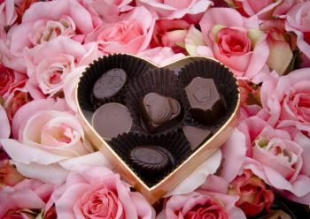 a heart-shaped box of chocolates on top of a bed of pink roses