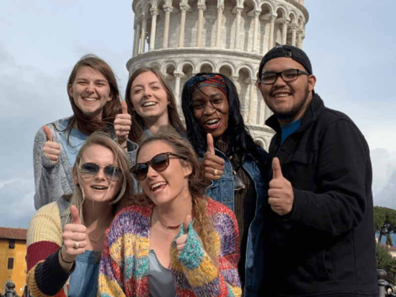 Six students pose with thumbs up in front of the Leaning Tower of Pisa
