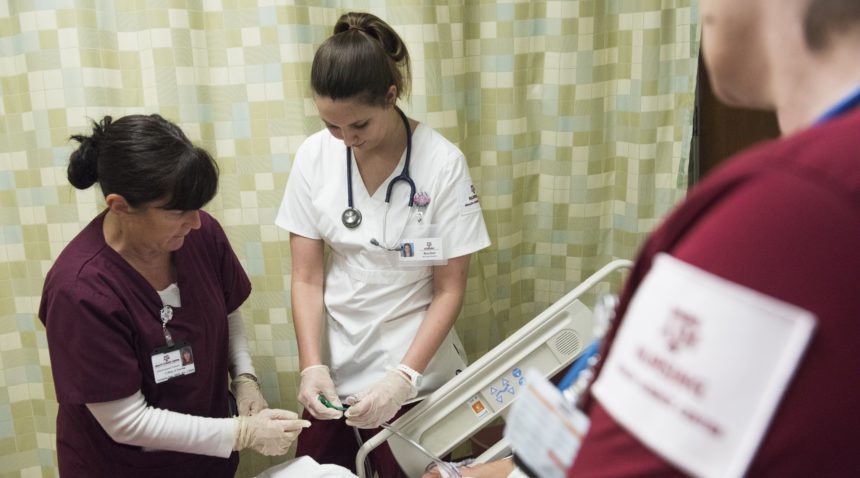 nursing student and teacher standing next to patient bed