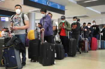 People standing with suitcases and wearing face masks in line at airport