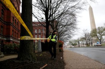 a police officer puts yellow caution tape around a tree in an area with the washington monument in the background