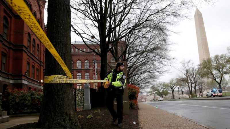 a police officer puts yellow caution tape around a tree in an area with the washington monument in the background