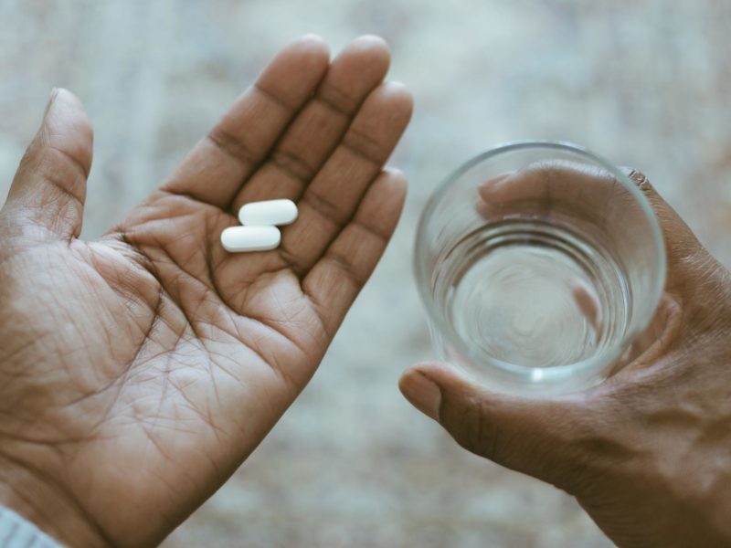 Close-Up View of Hands Holding Pills and Water