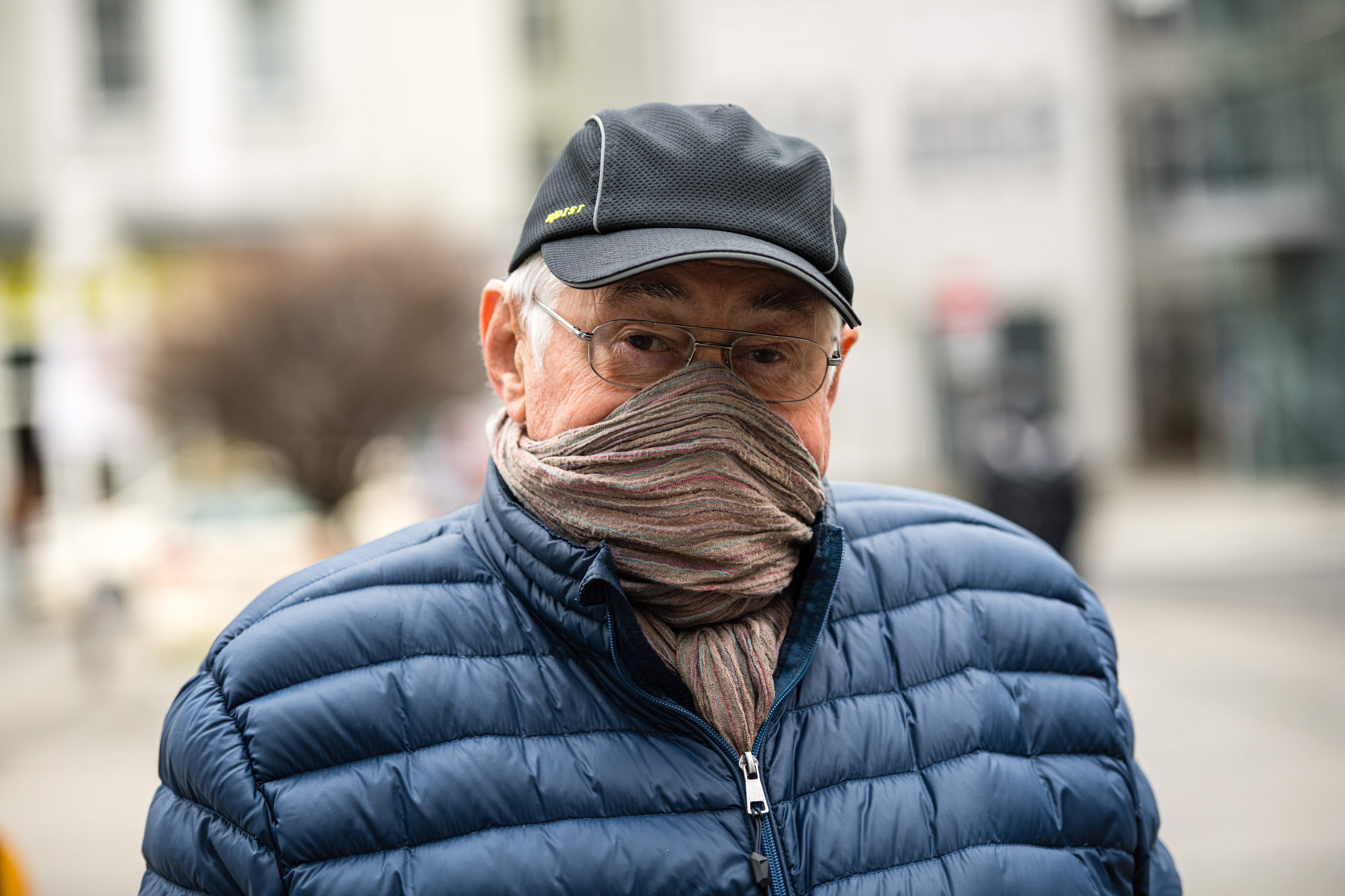 a mean wearing a hat and jacket with his scarf pulled over his mouth