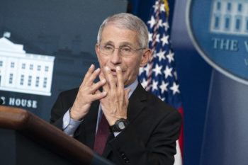 anthony fauci standing at podium holding his hands over his face