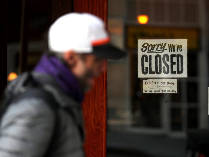 pedestrian walks by a restaurant with a closed sign on the door