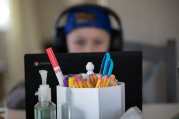 Photo of a child wearing a hat and headphones behind a computer screen at a desk with office supplies