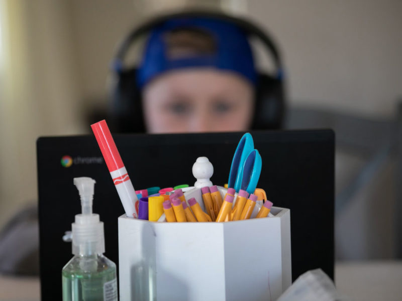 Photo of a child wearing a hat and headphones behind a computer screen at a desk with office supplies