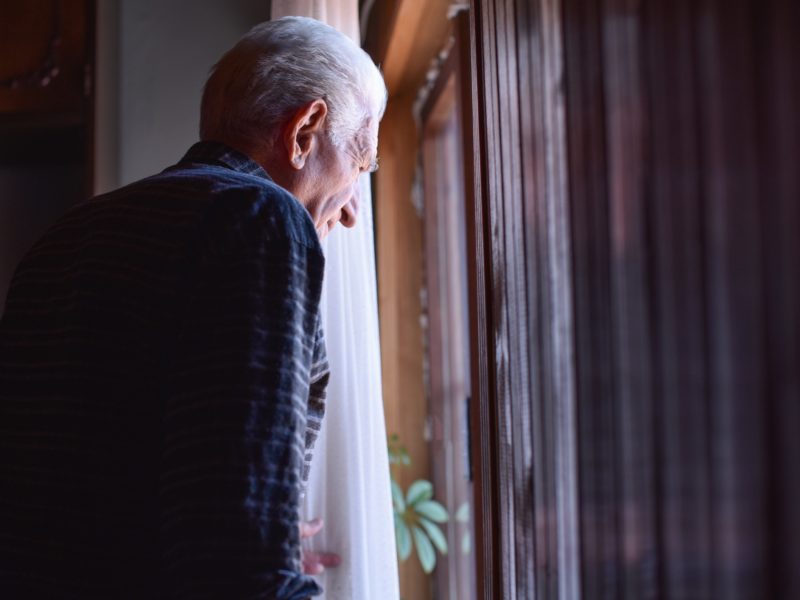 Senior man looking outside from home window