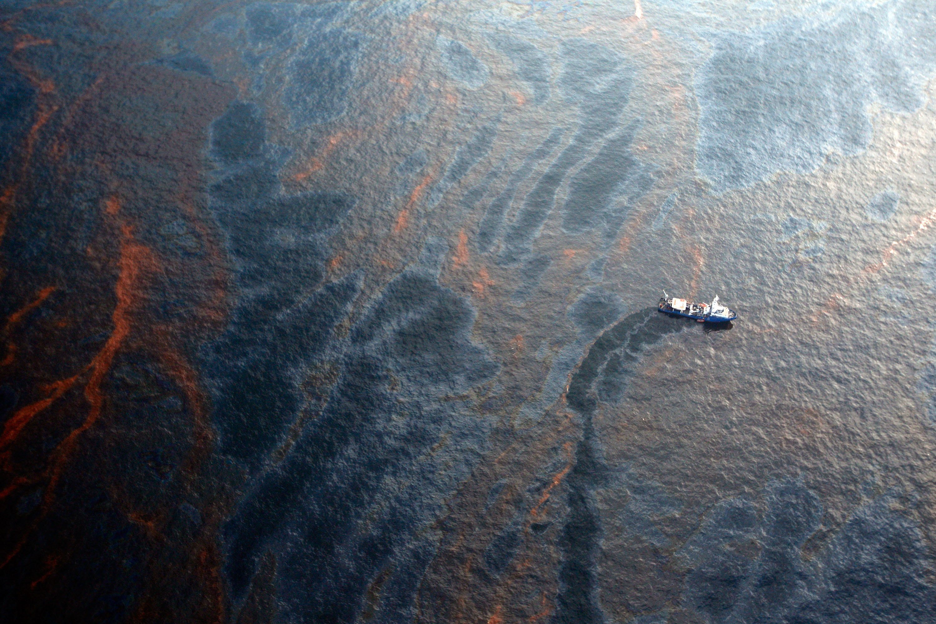 a boat drives through the fulf of mexico, with visible oil in the water