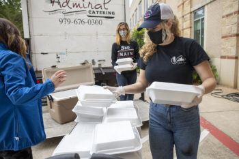 women wearing masks and gloves boxing up food in styrofoam containers