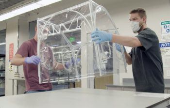 two lab technicians holding plastic isolation chamber