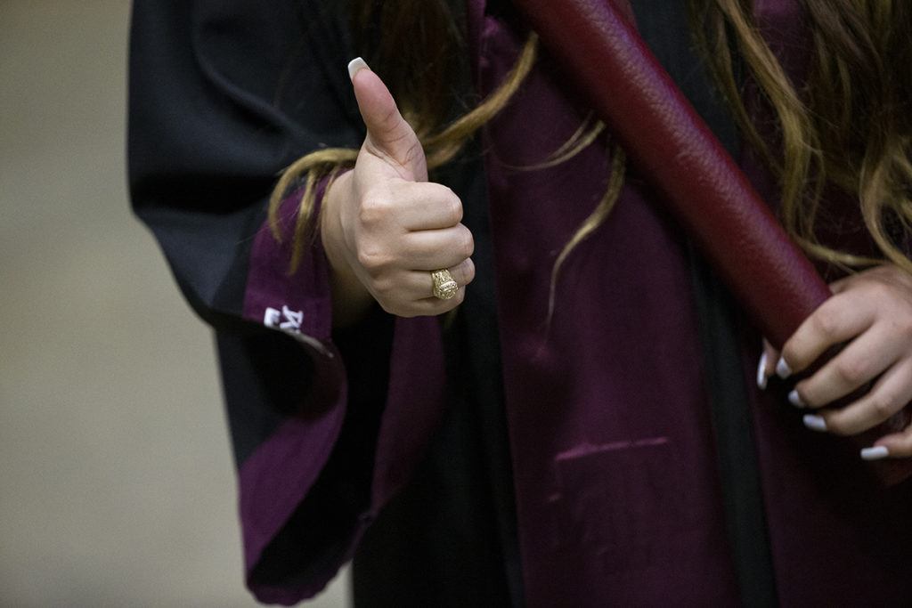 a photo of a woman's hand giving a Gig 'em and the other holding her diploma