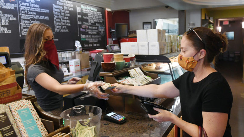 woman wearing face mask behind counter taking money from patron wearing face mask