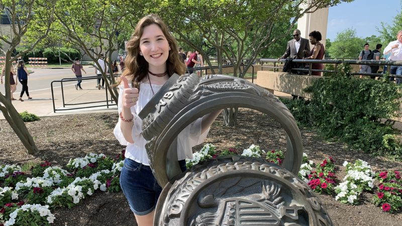 Sarah Venesky posting next to aggie ring sculpture on ring day