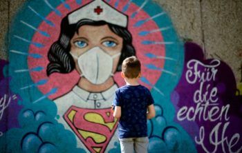 a boy stands in front of graffiti art featuring a nurse as superwoman