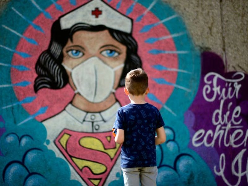 a boy stands in front of graffiti art featuring a nurse as superwoman