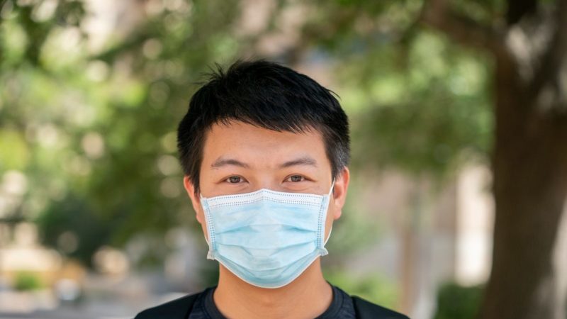 male student wearing blue face mask standing outside