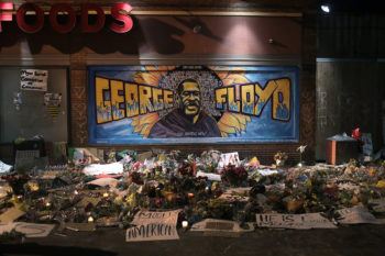a photo of a memorial to George Floyd, with flowers and signs of support below a mural of Floyd
