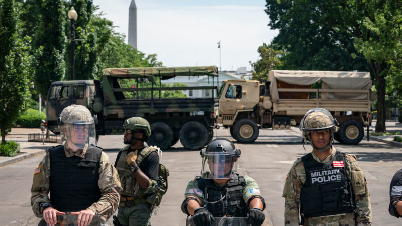 police officers and national guard vehicles block a street with the white house in the background