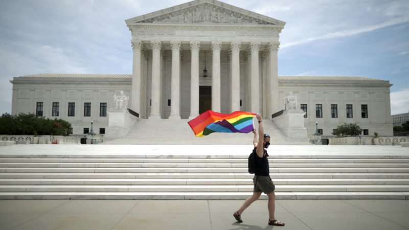 A man holding a Pride Flag walks in front of the U.S. Supreme Court building