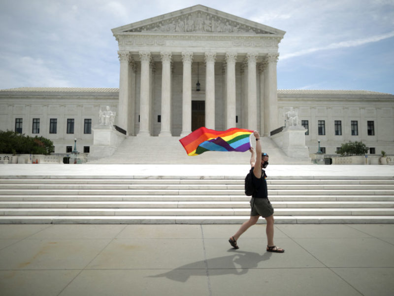 A man holding a Pride Flag walks in front of the U.S. Supreme Court building